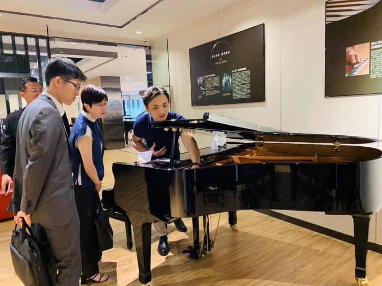 上海柏斯琴行有限公司華東區總經理吳福海（右一）向駐滬辦主任蔡亮（右二）介紹各種知名的鋼琴品牌
