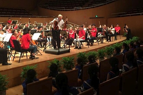 駐滬辦特別安排了二十多位新華小記者及二十位本地中學師生，於八月十一日下午到上海東方藝術中心觀摩樂團的總綵排，並與樂團指揮及青年樂手交流心得。圖示亞青樂團創辦人兼藝術總監龐信與二十多位新華小記者及二十位本地中學師生分享演出經驗，並為他們介紹管弦樂團成員所用的樂器。